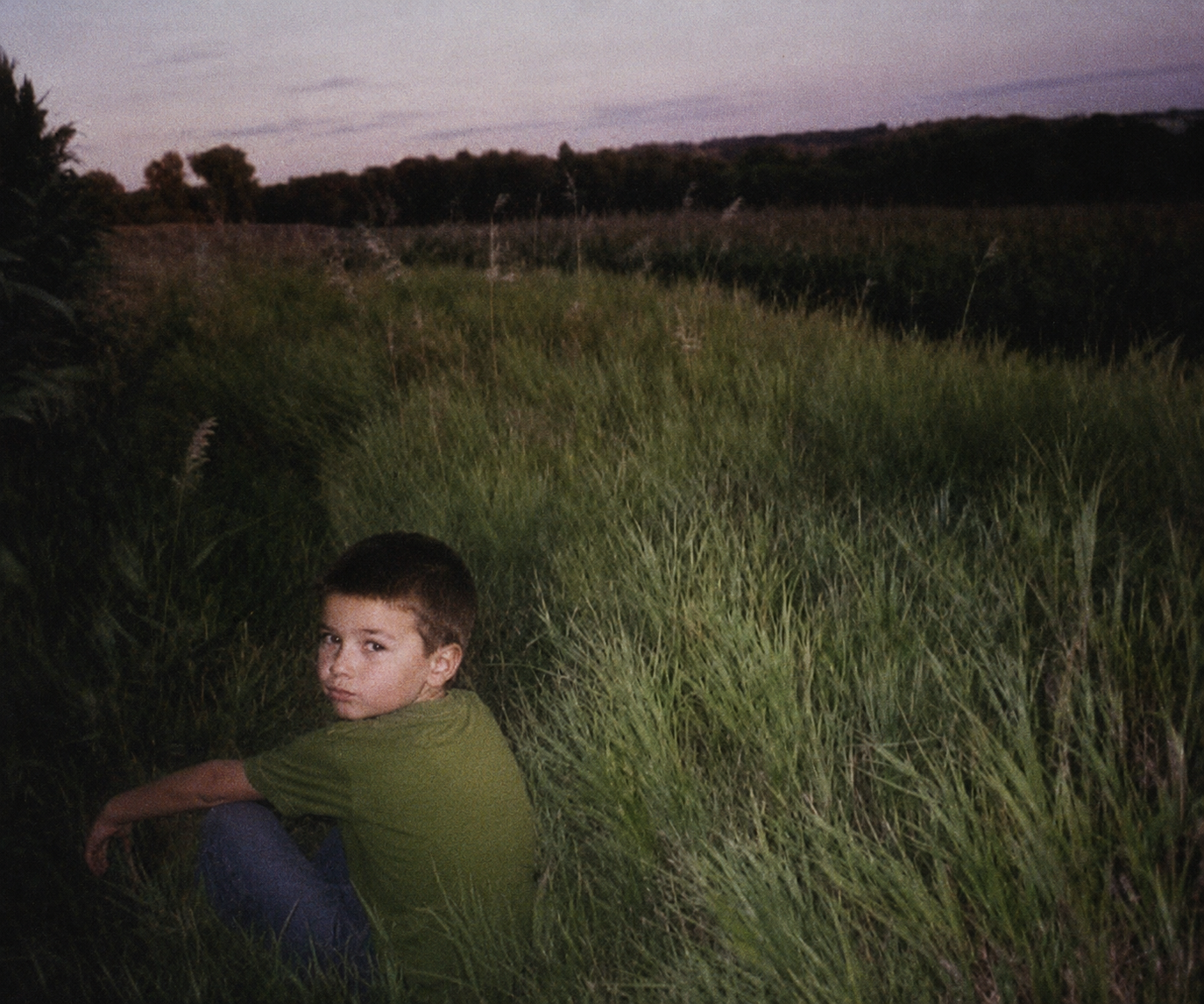 Sascha as a child sitting in a field at dusk